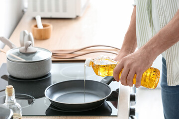 Man pouring sunflower oil on frying pan in kitchen - obrazy, fototapety, plakaty
