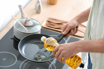 Man pouring sunflower oil on frying pan in kitchen