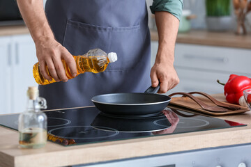 Man pouring sunflower oil on frying pan in kitchen