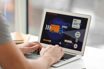 Young man using laptop with open page of delivery service application at home, closeup