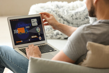 Young man using laptop with open page of delivery service application at home