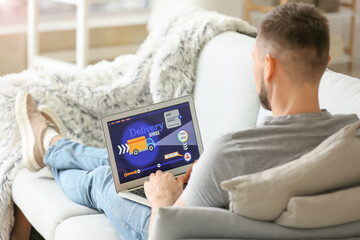 Young man using laptop with open page of delivery service application at home