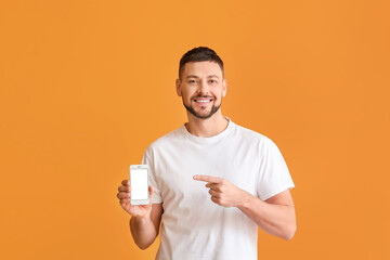 Young man pointing at mobile phone on color background