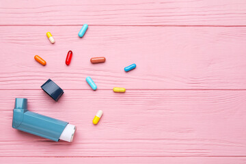 Modern inhaler and pills on color wooden background