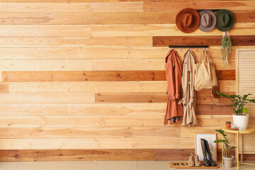 Hangers with clothes and hats on wooden wall