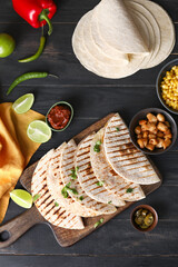 Board with tasty quesadillas on dark wooden background