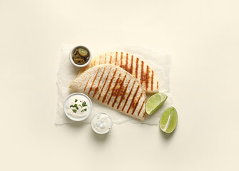 Parchment with tasty quesadillas, lime, sauces and pickled jalapenos on white background