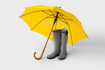 Stylish umbrella and rubber boots on light background