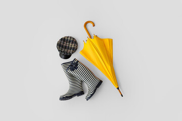 Stylish umbrella, rubber boots and hat on light background