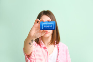 Young woman with covid-19 vaccination card on color background