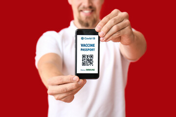 Young man with electronic immune passport on color background, closeup