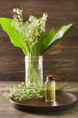 Bottle with essential oil and lily-of-the-valley flowers on wooden background