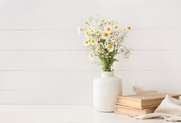 Fototapeta na wymiar Vase with beautiful chamomile flowers and books on light wooden background