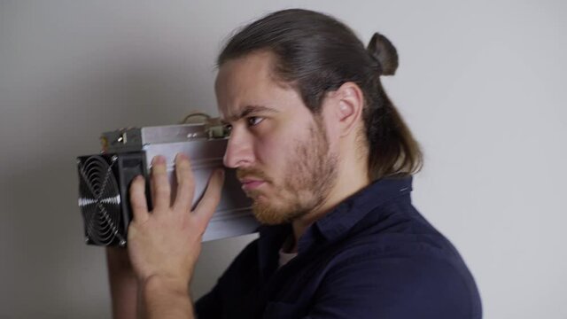 a man with a red beard in a blue shirt jokes, shoots an ASIC for mining, like a weapon