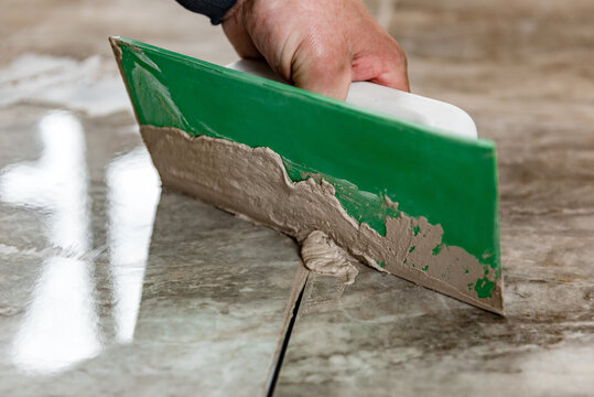 Grouting Ceramic Tiles. Tilers Filling The Space Between Tiles Using A Rubber Trowel.