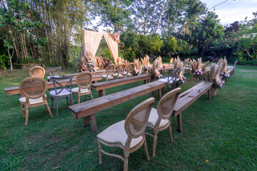A rustic garden wedding setup, with wooden chairs and benches, and a simple altar and aisle lined...