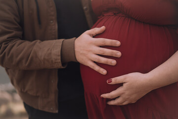hands on belly of pregnant woman dressed in red.