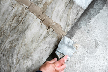 Applying a beige grout on the floor lined with tiles.