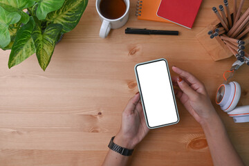 Above view woman holding mock up mobile phone on her workspace.