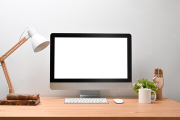 Modern Scandinavian home interior with mock up computer, lamp, coffee cup, books and plant on wooden desk.