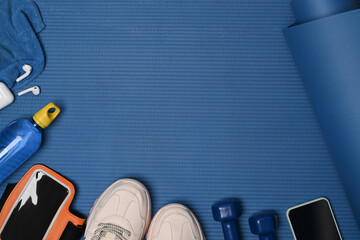 Above view fitness equipment and mobile phone on blue mat.