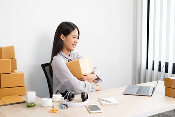 Obraz na płótnie Canvas Young Asian woman business owner with many parcel boxes on the table happy online sales job, use your laptop, get an order from customers, take notes, and make arrangements for delivery by post