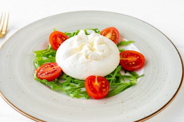 Salad with burrata cheese and cherry tomatoes on white wooden background