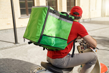 Rear view of a male courier in red uniform with thermo bag deliv