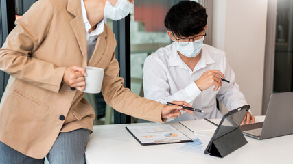 Naklejka premium Two colleagues wearing surgical masks analyzing the data in chart for marketing research
