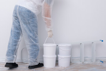 a man in protective clothing, bringing buckets of paint and a set of tools, against a white wall © kurgu128