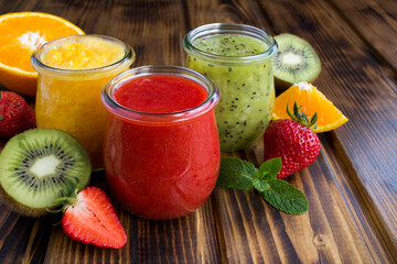 Different fruit smoothie or puree in the small glass jars on the wooden  background. Close-up.