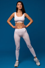 Fit woman in white activewear confidently posing on blue background