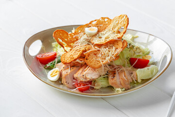 Caesar salad with grilled chicken on white wooden background