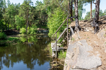 Fototapeta na wymiar A summer day in the woods. Fishing bridge with stairs on the rocky bank of the forest river.
