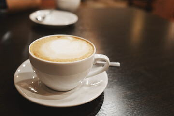a white cappuccino coffee cup with a heart - shaped pattern on the foam. a cup and saucer on a dark...