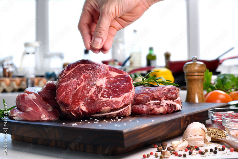 Canvas Prints hand sprinkling salt on fresh raw beef meat on a cutting board in the kitchen.