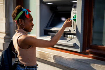 Beautiful african womn using ATM machine. Attractive young woman withdrawing money from credit card...