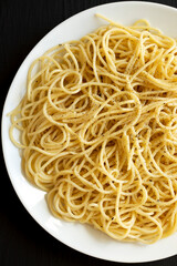 Homemade Cacio E Pepe Pasta with Pecorino Romano and Pepper on a white plate on a black surface, top view. Overhead, from above.