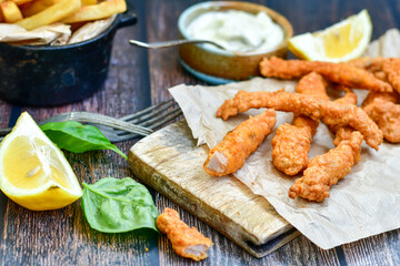 
 Crispy  deep fried   chicken strips  with sesame seeds and french fries . Breaded  with cornflakes chicken  breast fillets  with chilly peppers and fresh   basil on wooden rustic background