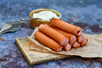 Classic boiled  and fried meat pork sausages on chopping board with pepper and basil and cherry tomatoes on wooden background. Snack for kids