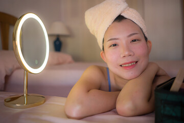 pretty Asian woman cleaning her face - lifestyle portrait of young happy and beautiful Korean girl at home applying makeup and facial beauty treatment looking to mirror