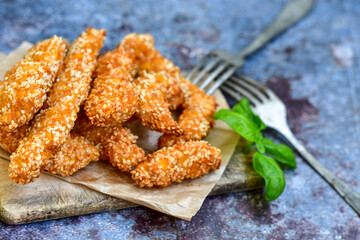 
 Crispy  deep fried   chicken strips  with sesame seeds and french fries . Breaded  with cornflakes chicken  breast fillets  with chilly peppers and fresh   basil on wooden rustic background