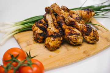 Fried chicken legs lie on a wooden board. Chicken shish kebab with a side dish of vegetables and green onions.