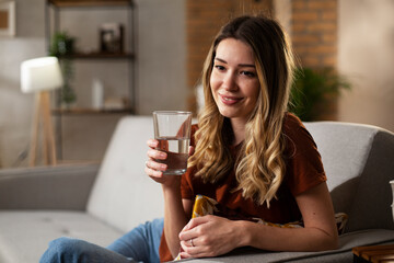 Beautiful young girl using the phone while drinkinng water. Portrait of smiling girl typing a message.