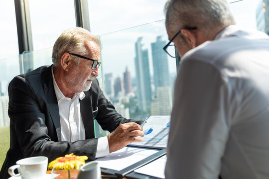 Two business men discussing idea in the office. One man is explaining while the other is listening. Both are wearing white shirt. The younger man is wearing tie and glasses.