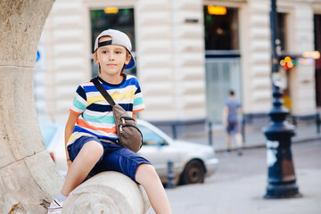 Cute fashionable boy walking the city. Happy child wearing trendy casual clothes and waist bag.