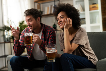 Boyfriend and girlfriend drinking beer at home. Happy couple watching sports game on tv..