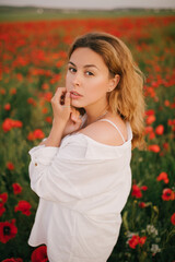 Young beautiful woman wearing white linen suit posing in a poppy field.