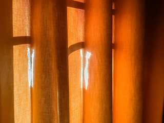 Close-up view of broken old curtain in vertical folds. Bright orange curtain made with dense fabric. Tear marks of fabric on curtain.