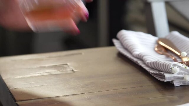 Woman Picks Up Stemless Wine Glass Of Rose Half-Full From Wooden Table, Closeup Of Hand Wearing Pink Nail Polish And Kitchen Table Napkin And Silverware In Background, White And Golden Red Color